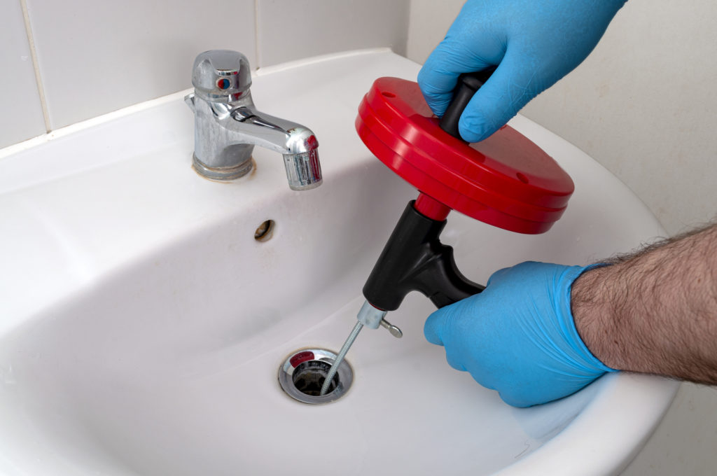 A handyman's gloved hands inserting a drain snake into a bathroom sink