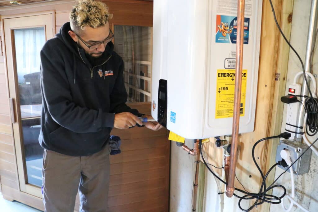 Plumber in Mattioni hoodie using a screwdriver on a tankless water heater