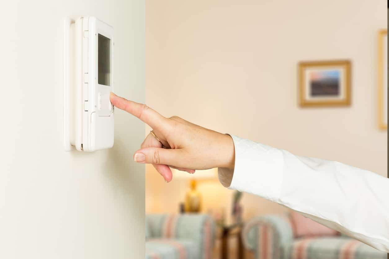 female hand pressing button on a modern electronic thermostat timer on wall with focus on the screen and fingers of the woman