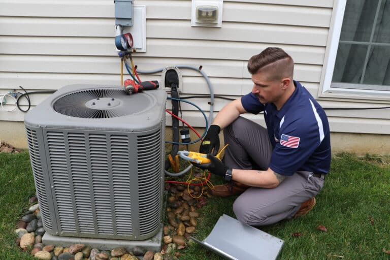 mattioni plumbing heating cooling technician kneeling next to hvac unit looking at inspection tool